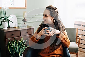 Dreamy young woman savoring warm coffee in cozy home interior. Beautiful lady enjoying a hot drink while relaxing at home. Serene