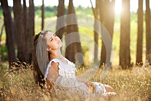 Dreamy young woman sitting in field with sunlight in background