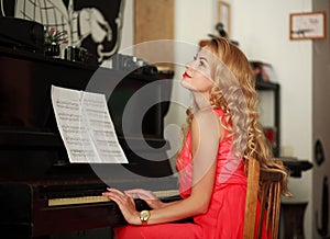 Dreamy young woman sitting at the piano in the room