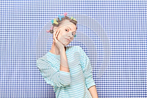 Dreamy young woman with skincare product on face, with hair curlers