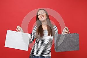 Dreamy young woman in striped clothes looking up, holding packages bags with purchases after shopping isolated on red