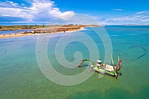 Dredger boat excavating sand for beach in shallow water near town of Nin