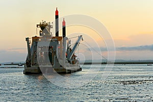 Dredging vessel operating at sunset. photo