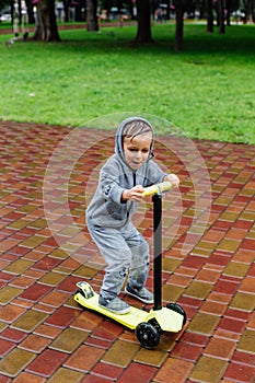 Drenched in the rain, a boy in a sport suit skates on a scooter. Spring walk in the city park, rainy weather