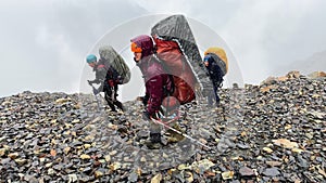 Drenched tourists with large backpacks walk on slippery stones in heavy rain.