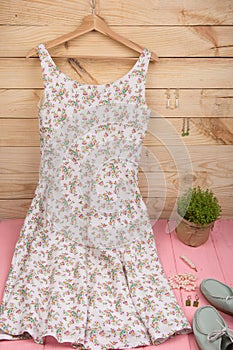 dress in floral print on hangs on hanger, blue shoes and pearl jewelry: necklace, hair pearl clip, earrings on wooden background
