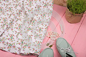 dress in floral print on hangs on hanger, blue shoes and pearl jewelry: necklace, hair pearl clip, earrings on wooden background