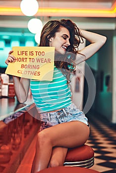 Dress to impress. an attractive young woman holding up a sign in a retro diner.