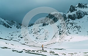 Dressed bright orange jacket backpacker man with trekking poles and backpack trekking by the mountain valley during high altutude