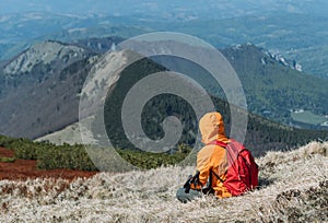 Oblečená jasne oranžová bunda s turistickými palicami sediac na kopci a užívajúc si zelené údolie v pohorí malá fatra