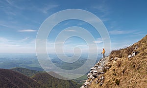 Oblečená jasně oranžová bunda batohem s trekovými holemi na skalnatém útesu těší zelené údolí na pohoří malá fatra