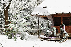 Dressed Christmas tree, old wooden cottage and Santa Claus sleigh in a tranquil winter forest.