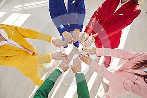 Dressed in colorful fashionable business suits team joins hands to create circle concept of unity and teamwork. Team in photo