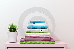 On the dresser there is a stack of clean ironed bed linen, folded multi-colored towels and a home plant stands