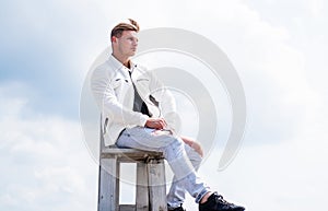 Dressing both casually and fashionably. Handsome guy wear casual style outdoors. Man sit on chair on cloudy sky. Casual