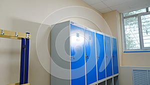 Dressing room in gym with boxes for clothes and keys in lock. Multiple closed lockers are visible in background. School