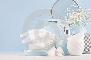 Dressing table with circle mirror, cosmetic silver accessories and white small flowers in ceramic pastel blue vase on white wood.