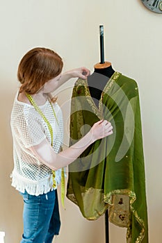 Dressmaker with measuring tape draping cloth on mannequin and in sewing studio
