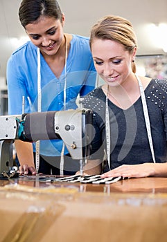 Dressmakers unite. two seamstresses working on a new design inside their fabric shop.