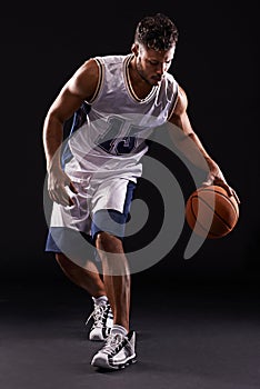 Dribbling pro. Studio shot of a basketball player against a black background.