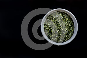 Dried aonori seaweed flakes in pot on dark