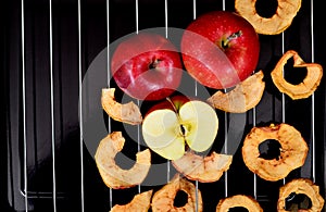 Dried apple chips and red apple on a metal grill and black background