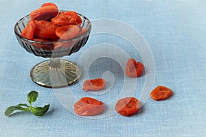 Dried apricots in a glass vase with a mint branch on a blue background , side view, close-up-the concept of the usefulness of