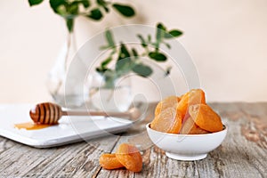 Dried apricots and honey in white plate on wooden table. Dehydrated fruits. Healthy sweets concept