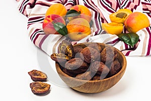 Dried apricots in the wooden bowl, fresh leaves and fruits on tablecloth on white background. Natural, organic dried apricot fruit