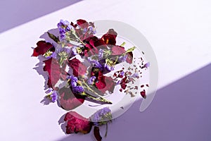 Dried blue flowers and rose petals on the purple background