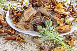 Dried brown pear slices white plate with white flowers. White daisy flowers and a green wormwood branch. Useful dry food. Edible s