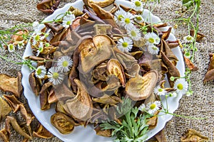 Dried brown pear slices white plate with white flowers. White daisy flowers and a green wormwood branch. Useful dry food. Edible s