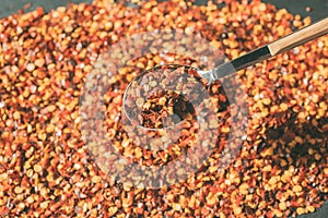 Dried chili flakes on wooden spoon. Close up view of crushed red cayenne pepper. Top view of dried red chili flakes.