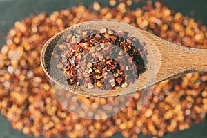 Dried chili flakes on wooden spoon. Close up view of crushed red cayenne pepper. Top view of dried red chili flakes.