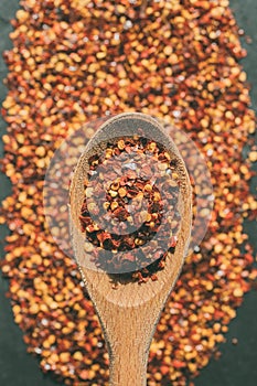 Dried chili flakes on wooden spoon. Close up view of crushed red cayenne pepper. Top view of dried red chili flakes.