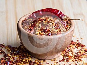 Dried chili pepper flakes in wooden bowl on the wooden table. Dried and crushed fruits of Capsicum frutescens, used as