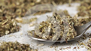 Dried chopped medicinal herb wormwood falls into a spoon in slow motion.