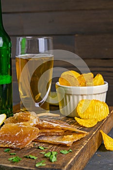 Dried cod fillet with beer, lemon and potato chips on dark wooden board. Snack on fish with beer. Front views, close-up