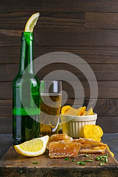 Dried cod fillet with beer, lemon and potato chips on dark wooden board. Snack on fish with beer. Front views, close-up
