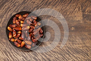 Dried dates in a black plate on a wooden brown background. Dried fruit with copy space. Top view, flat lay