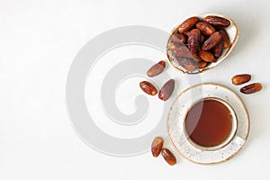 Dried dates in a bowl and a tea drink on white background with copy space. Traditional Arabic sweets. Popular food for Ramadan.