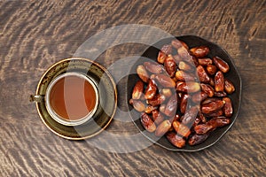 Dried dates in a plate and a cup of tea on a wooden background. Popular food for Ramadan. Top view, flat lay