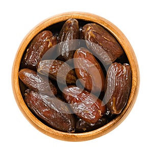 Dried Deglet Nour dates in wooden bowl over white