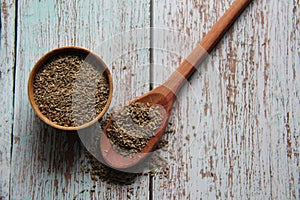 Dried fennel seeds, in a wooden bowl with a wooden spoon.