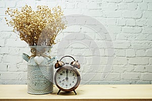 Dried flower in metal vase and alarm clock with space copy on white brick wall background