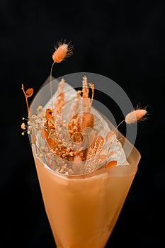 Dried flowers arragement wrapped in paper on dark background in woman's florist hand