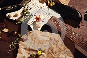 Dried flowers and electric guitar on rare music notes on wooden background closeup