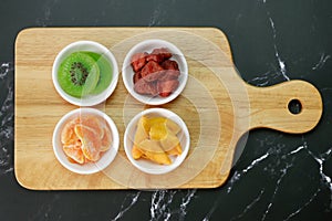 Dried fruits, with kiwi slices, strawberry, dried mango slices, orange, and prunes in white bowls on wooden plate. Organic healsy