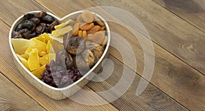 Dried fruits mix baner in wooden heart shape box isolated on wooden background. Top view of various dried fruits figs, apricots,