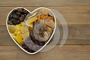 Dried fruits mix, in wooden heart shape box isolated on wooden background. Top view of various dried fruits figs, apricots, mango
